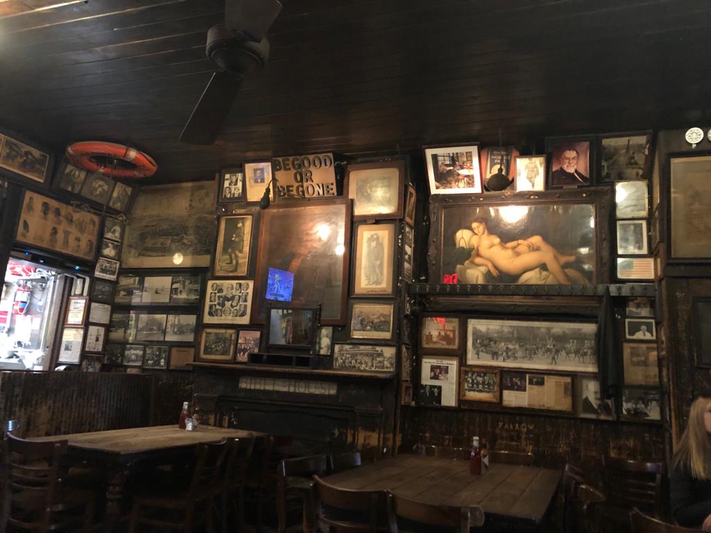 Wall of historic photographs, framed memorabilia and newspaper clippings inside McSorley's Old Ale House, showing how traditional Irish pubs preserve history through everyday objects.